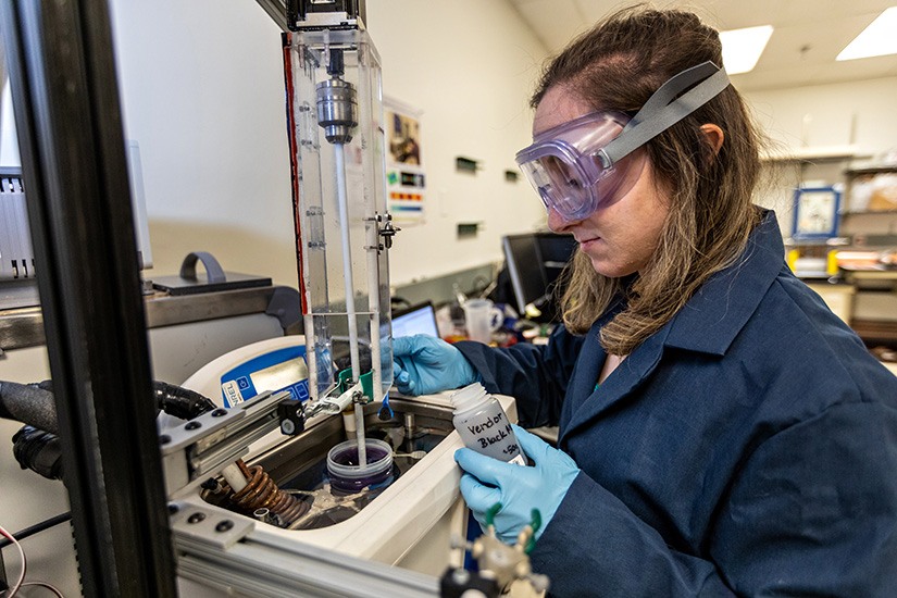 A researcher wearing protective goggles and gloves works in a laboratory.